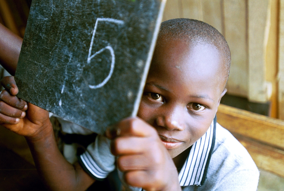 Child holding up number 5 on a chalkboard