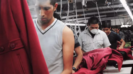 The image shows a man in a factory steaming a red coat